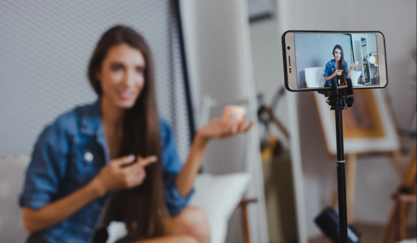 A young woman filming herself with a smartphone on a small tripod.