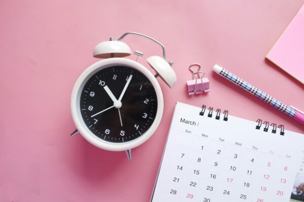 A clock and a calendar on a pink background to symbolize organization.