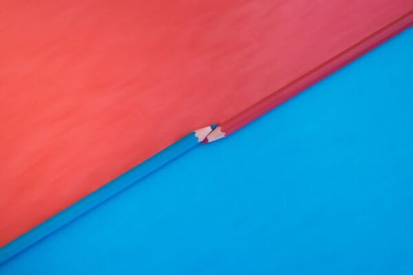 Two vibrant pink and blue colored pencils with the tips touching on a matching background with opposite colors. Top down view flat lay with empty space for text.