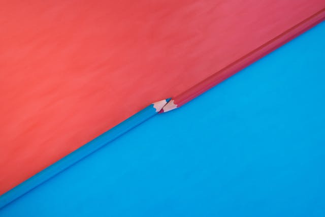 Two vibrant pink and blue colored pencils with the tips touching on a matching background with opposite colors. Top down view flat lay with empty space for text.