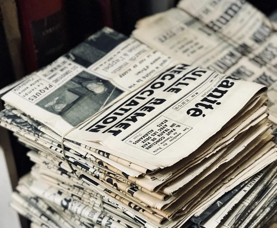 Stack of out of date newspapers stacked on top of each other. Most are torn and dirty.